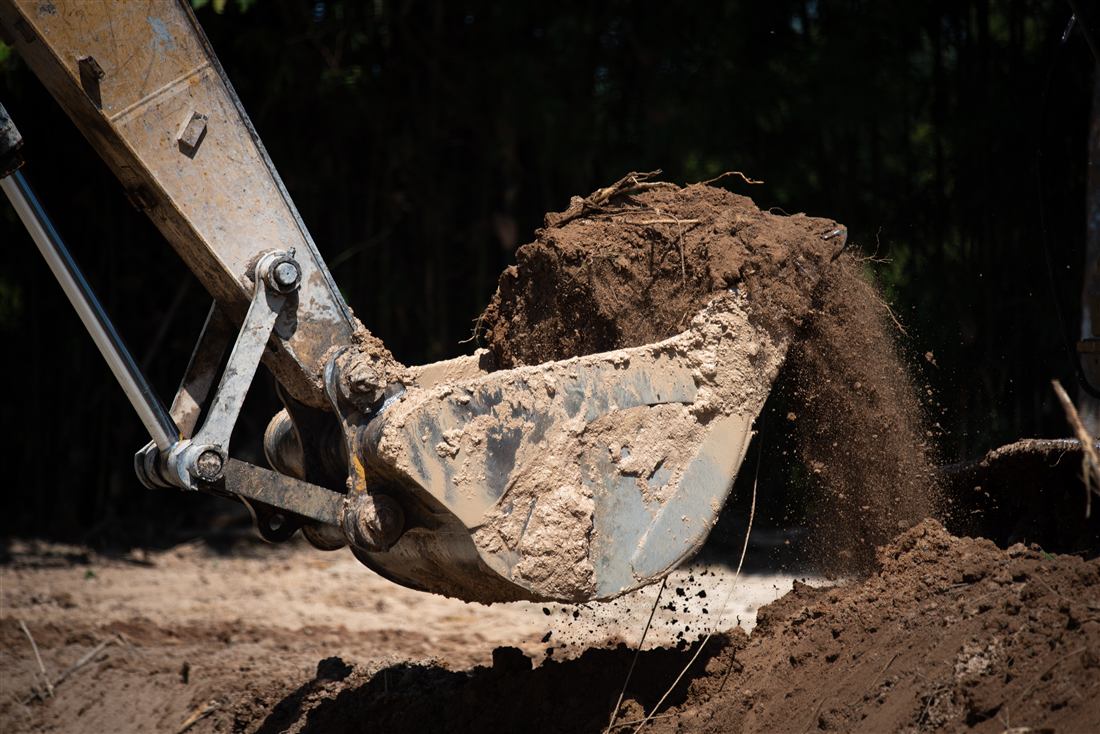 Excavator bucket moving soil on a cleared lot